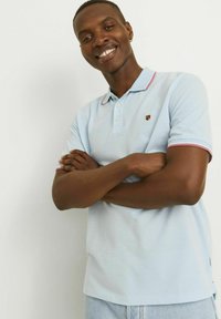 Polo shirt azzurro chiaro con una finitura testurizzata, colletto e bordi delle maniche in contrasto rosa e bianco, caratterizzato da un piccolo logo sul petto.