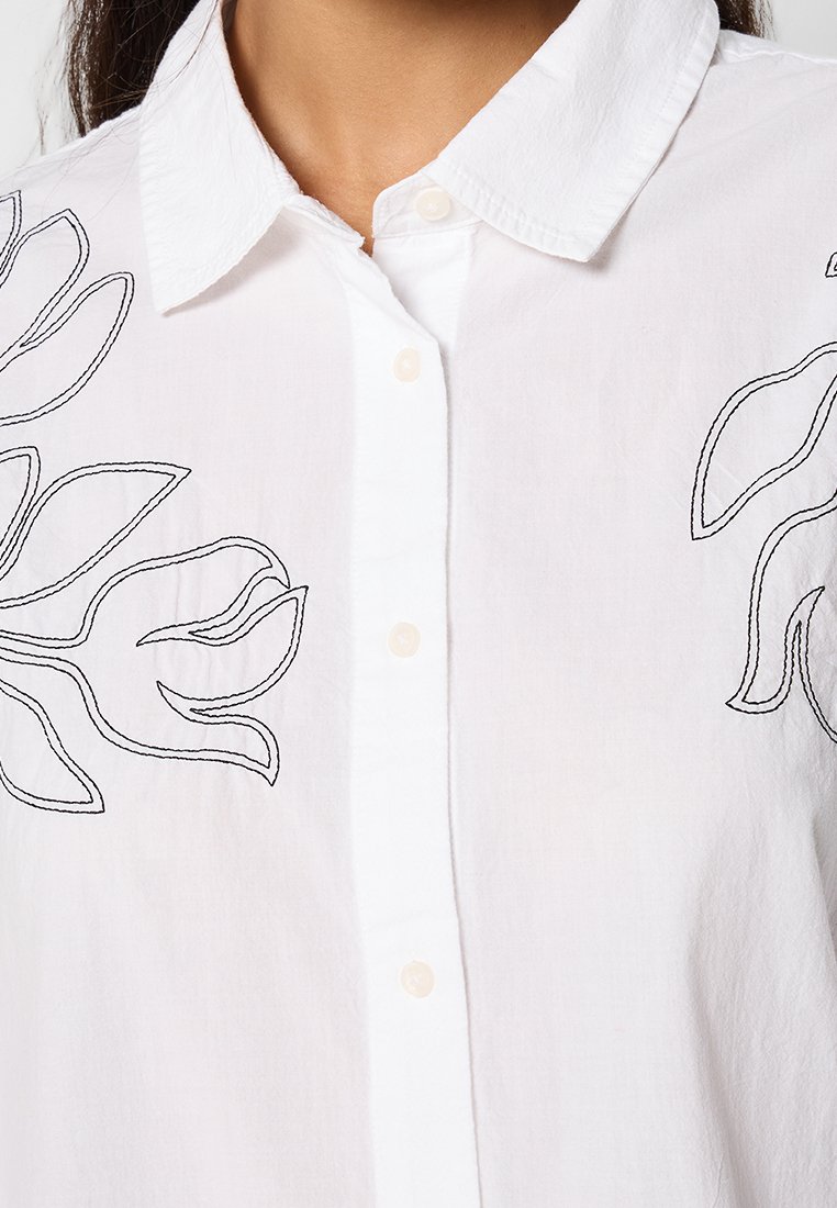 Witte overhemden gemaakt van lichtgewicht stof, met zwarte bloemmotieven borduurwerk aan de linkerkant en een klassiek kraagontwerp.