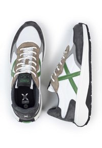 Zapatillas blancas y grises con acentos verdes. Presentan materiales de ante y malla, puntera redonda y suela de goma contrastante. Diseño con cordones.
