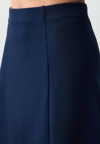Gonna blu navy realizzata in tessuto liscio, con vita aderente e un design semplice caratterizzato da linee pulite e una leggera lucentezza.