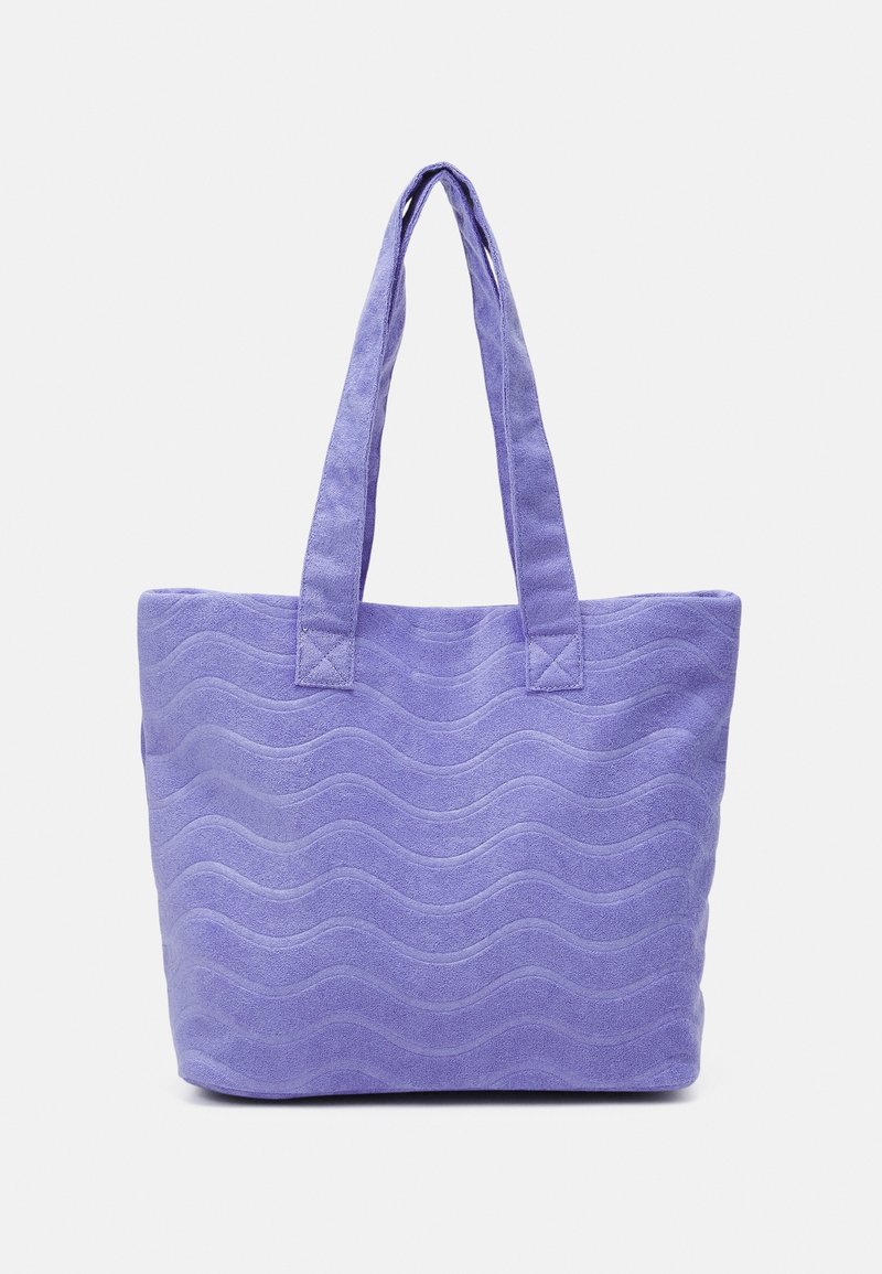 Sac cabas violet lavande avec un motif texturé ondulé et deux longues anses, debout sur un fond uni.