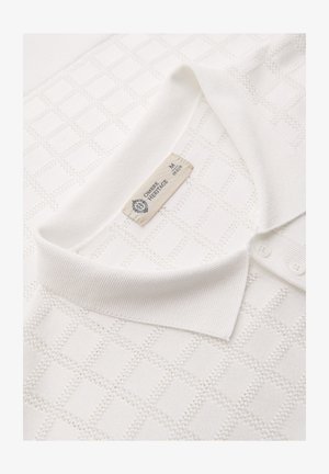 Polo en maille texturée blanche avec col côtelé, trois boutons et une étiquette en tissu indiquant « OMBRE HERITAGE M 48 EUR ».