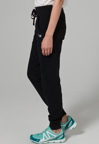 Pantalones jogger negros con cinturilla elástica y cordón, que cuentan con bolsillos laterales y un pequeño logo. Combinados con zapatillas deportivas en color verde azulado.