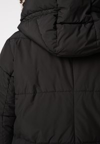 Zwarte pufferjas met capuchon, geruite ontwerp en gladde textuur. Achteraanzicht toont stiksel details en afgeronde rand van de capuchon.