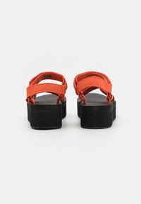Orange remsandaler med en svart plattformsbas. Har texturerad gummisula och justerbara remmar för en säker passform.