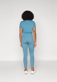 Teal treningssett som består av en tettsittende kortermet topp og høytlivs leggings med et subtile blomstermønster, kombinert med hvite treningssko.