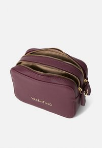 Trousse de maquillage en cuir bordeaux avec deux compartiments zippés, quincaillerie dorée, fond plat et logo "VALENTINO" en relief.