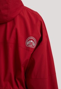 Veste imperméable rouge avec capuche, arborant un logo de montagne blanc et le texte « JACK1T » sur la partie supérieure de l'épaule arrière.