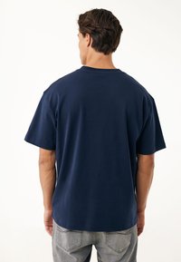 Camiseta de algodón azul marino con cuello redondeado, mangas cortas y un corte relajado. Textura suave, diseño minimalista, sin patrones visibles.