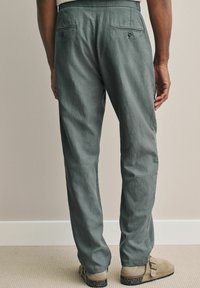 Grå bukser med en afslappet pasform, baglomme og tekstureret stof, parret med beige slip-on sko med en pletmæssig sål.