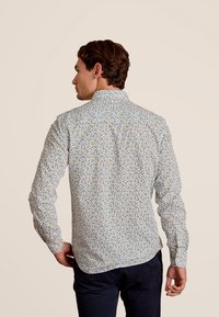 Wit katoenen overhemd met lange mouwen, voorzien van een kleurrijk abstract patroon, knoopsluiting en gebogen zoom, gezien van de achterkant.