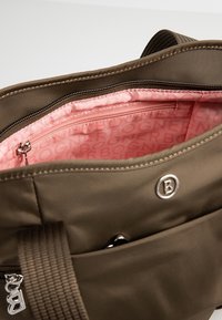 Sac en tissu vert olive avec une fermeture éclair. L'intérieur est doté d'une doublure rose avec un motif de logo répété et une poche zippée supplémentaire.