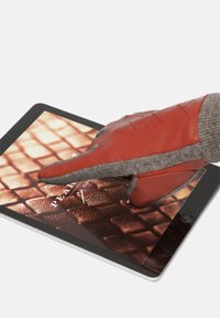 Crvena kožna rukavica s sivim pletenim rukavom dodiruje zaslon tableta koji prikazuje teksturirani uzorak. Tablet ima elegantni crni okvir.