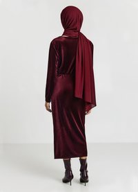 Bordeaux Samtkleid mit langen Ärmeln und passendem Hijab. Figurbetonte Silhouette, knielang, kombiniert mit High-Heel-Stiefeln.