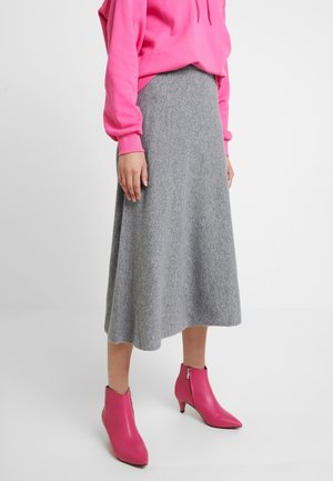 Jupe midi en laine grise associée à un sweat à capuche rose. Le modèle porte des bottes de cheville roses avec un bout pointu et une fermeture éclair. Texture lisse dans l'ensemble.