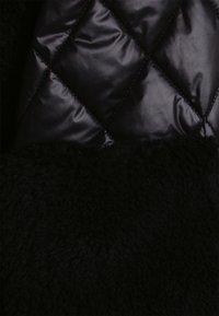 Svart vadderad jacka med glansigt material och diamantmönster; nederdelen i plysch, texturerad svart tyg.