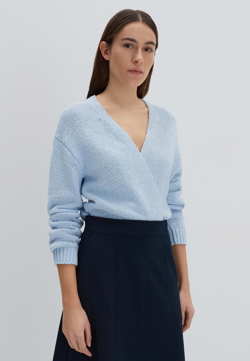 Pull en tricot bleu clair avec un décolleté en V profond et des manches longues, associé à une jupe bleu marine foncé. Tissu texturé avec une coupe décontractée.