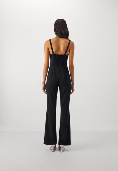 Tutina nera con corpino aderente, spalline regolabili e gambe svasate. Texture liscia e zip nascosta sul retro.