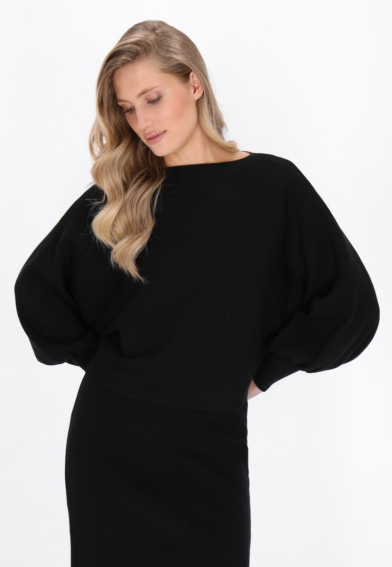 Schwarzer gestrickter Pullover mit übergroßen Ärmeln und einem breiten Halsausschnitt, kombiniert mit einem taillierten schwarzen Rock. Glatte Textur, minimalistisches Design.