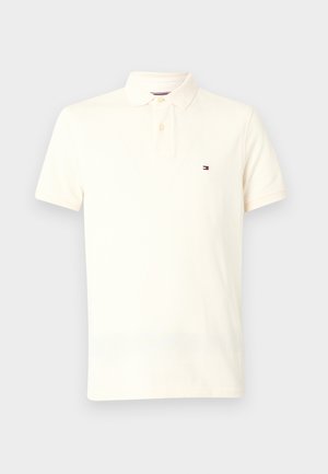 Kreminės spalvos polo marškiniai, pagaminti iš medvilnės, su klasikiniu apykakle, dviem mygtukais, trumpomis rankovėmis ir mažu logotipu kairėje krūtinės pusėje.