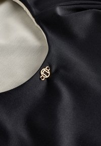 Gros plan d’un tissu lisse noir et beige avec un petit emblème rond en or attaché près de la couture du tissu.