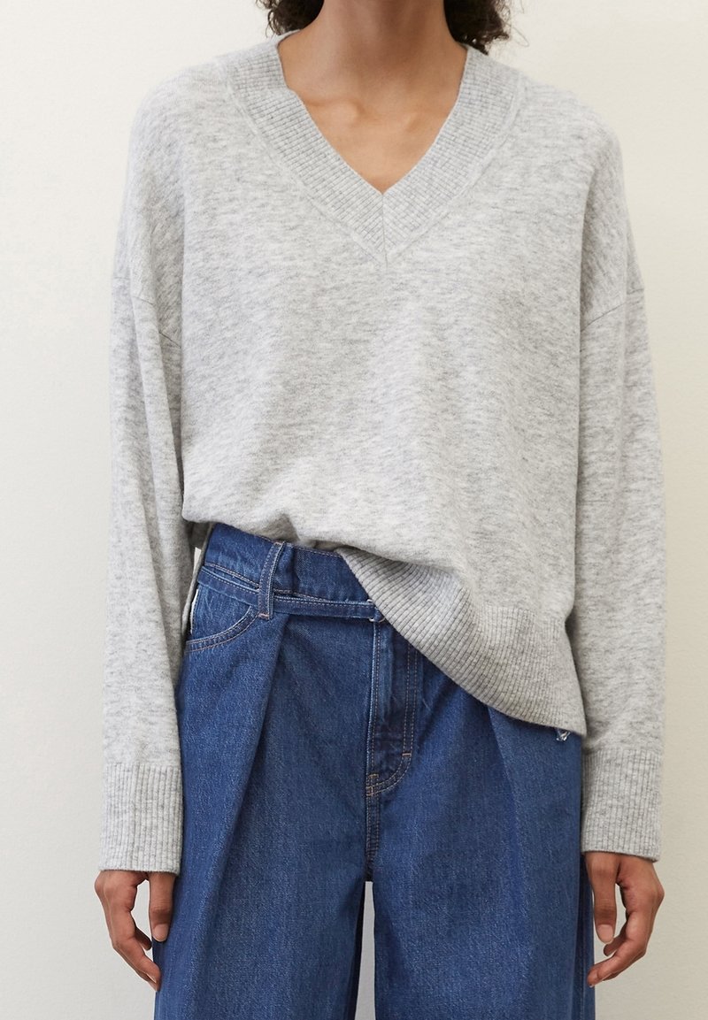 Maglione grigio chiaro a maglia con scollatura a V profonda, maniche lunghe e polsini a costine, abbinato a jeans a palazzo blu in denim a vita alta.