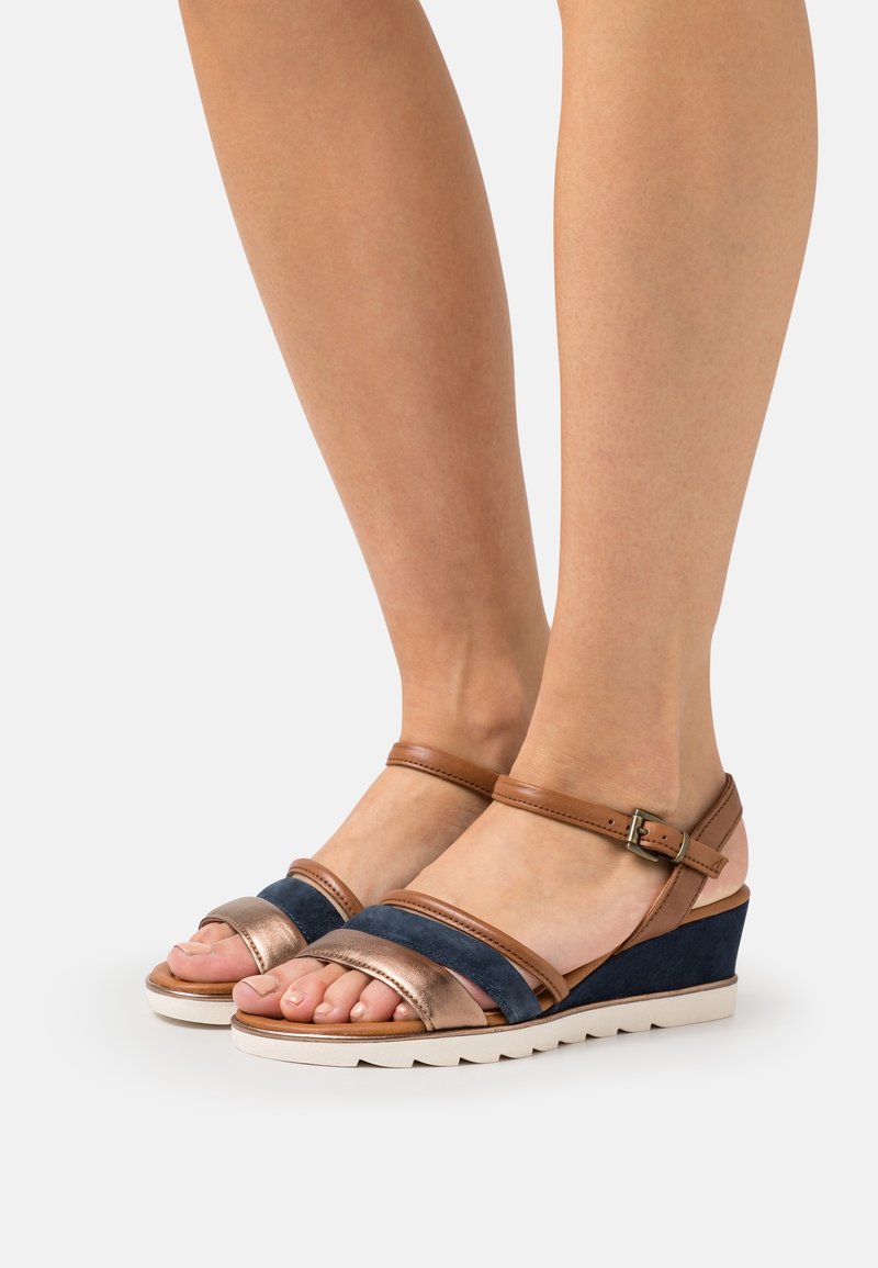 Sandales compensées marron et bleu marine avec doubles brides en cuir et suède, dotées d'une semelle texturée et d'une boucle à la cheville pour un ajustement.