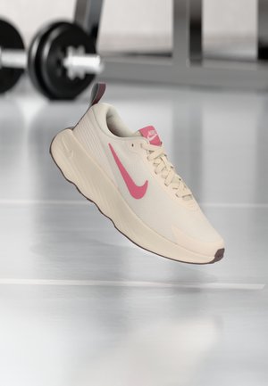 Scarpa da ginnastica beige con swoosh Nike rosa, tomaia in mesh strutturato, suola beige e dettagli marroni, progettata per comfort e prestazioni.