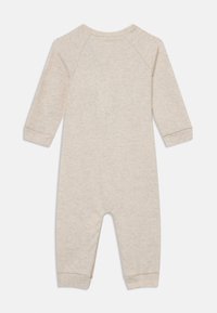 Une grenouillère en coton beige avec de longues manches raglan, des poignets côtelés, une fermeture à pression au niveau du cou, et une texture douce pour le confort.