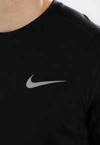 Czarna sportowa koszulka z okrągłym dekoltem, wykonana z gładkiego materiału, z odblaskowym srebrnym logo Nike na piersi.