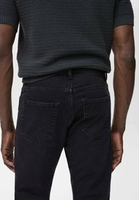 Ciemnoniebieskie dżinsy o slim fit, z dwoma tylnymi kieszeniami. Tkanina ma gładką teksturę i lekką elastyczność, z czystym wykończeniem.