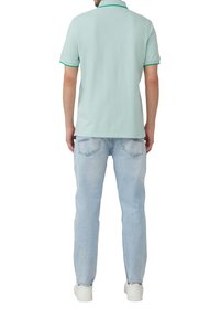 Polo verde menta a maniche corte con colletto, contrastato da rifiniture verdi; abbinato a jeans azzurri e sneakers bianche.