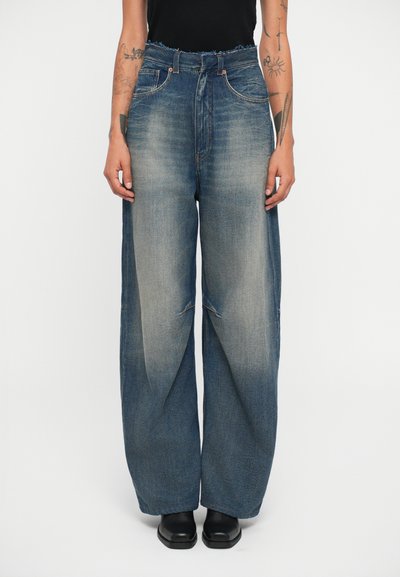 Jeans o szerokich nogawkach w średnim niebieskim kolorze, z przetartym wykończeniem, postrzępionym paskiem i kieszeniami z przodu. W połączeniu z czarnymi botkami za kostkę.