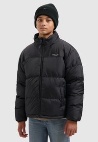 Zwarte pufferjas met een hoge kraag, ritssluiting en gestikte vulling. Gecombineerd met denim jeans en een zwarte beanie.