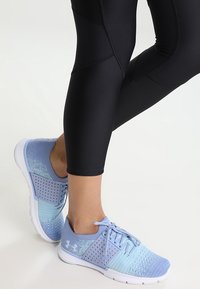 Jasnoniebieskie buty sportowe z przewiewną siateczką i perforowanym wzorem. Biała podeszwa z wiązaniem, zestawione z czarnymi legginsami.
