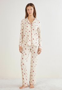 Bawełniane piżamy w kwiatowy wzór w odcieniu kremowym z czerwonymi akcentami; zawierają koszulę zapinaną na guziki oraz długie spodnie z elastycznym paskiem w talii.