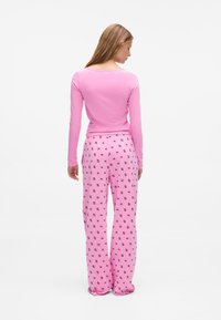 Roze lange mouw top en pyjamabroek met een herhalend zwart kattenpatroon. De stof is zacht en de broek heeft een losse pasvorm met een elastische taille.