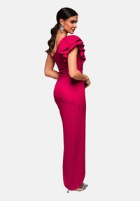 Robe de soirée fuchsia avec des épaules à volants, silhouette ajustée et texture lisse. Associée à des talons métalliques.