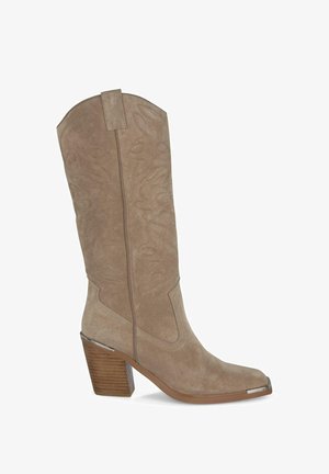 Botte de cowboy en daim beige avec un bout pointu, des coutures décoratives sur la tige et un talon bloc avec un accent en métal sur le bout.