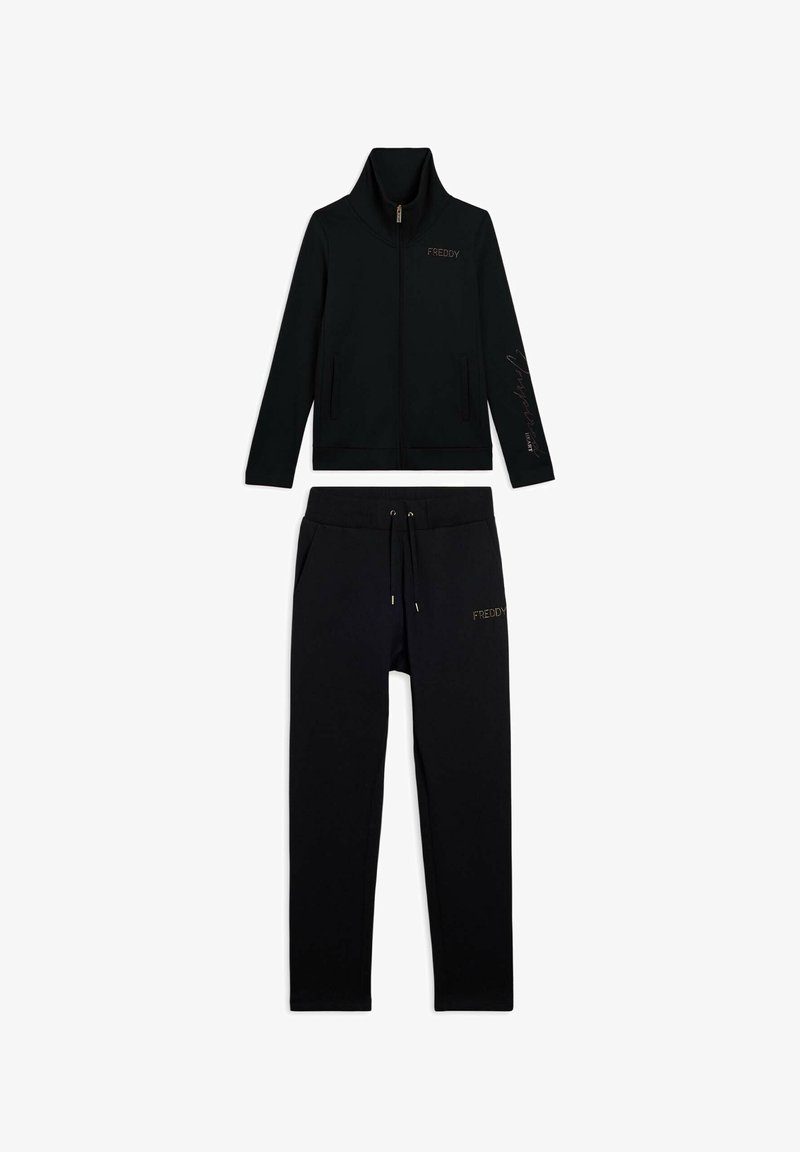 Chaqueta negra con cremallera y cuello alto, y pantalones a juego con cordones, ambos con la marca "FREDDY" en el pecho y en el muslo.