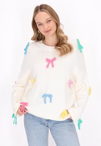 Weißer Strickpullover mit bunten Filzschleifen in Pink, Blau, Gelb und Grün, mit langen Ärmeln und rundem Ausschnitt.