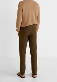 Bruine trui, olijfgroene broek, casual pasvorm. De broek heeft zijzakken, de zoom zit iets boven de enkel en wordt gedragen met sandalen.