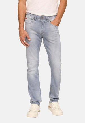 Jean en denim bleu clair avec une coupe slim, un design à cinq poches et une fermeture à bouton. Assortis avec des baskets blanches et une chemise neutre.