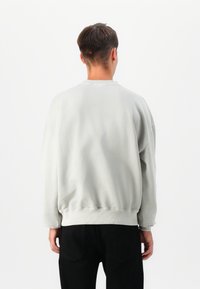 Sweatshirt cinza claro, ajuste solto, com bainha e punhos canelados. Textura suave, decote redondo e design descontraído. Usado com calças pretas.
