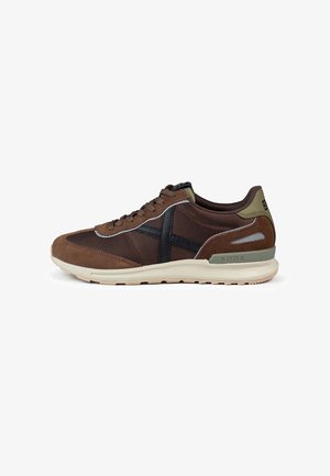 Chaussures de sport en daim brun et mesh avec des détails noirs, une semelle rembourrée et un accent vert au niveau du talon. Design classique à lacets.
