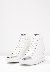 Baskets montantes blanches avec un côté texturé, un embout en métal argenté et des lacets blancs. Dotées d'une étiquette noire de marque sur la languette.