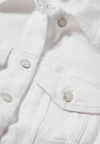 Chaqueta de mezclilla blanca con botones a presión plateados, doble bolsillo en el pecho y costuras visibles. Textura suave con un diseño estructurado.