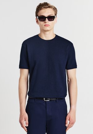 Navy blue short-sleeve knitted t-shirt with a round neckline, paired with dark trousers and black sunglasses, showcasing a smooth texture.