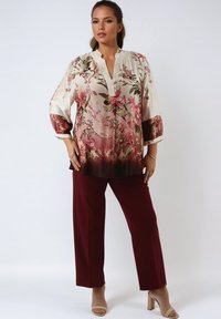 Flowy, floral blouse in soft silk with pink and green patterns, featuring a v-neck and three-quarter sleeves, paired with burgundy trousers.