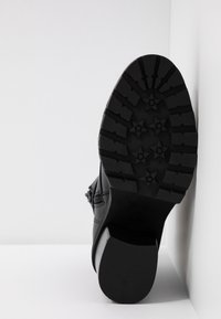 Svart läderstövel med en texturerad gummisula. Har en kraftig klack och blixtlås på sidan. Sulan har ett stjärnformat mönster.